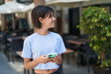 Adorable hispanic girl smiling confident using smartphone at street