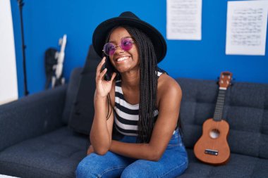 Afrikalı Amerikalı kadın müzisyen gülümsüyor. Müzik stüdyosunda akıllı telefondan konuşuyor.