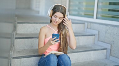 Okulda akıllı telefon ve kulaklık kullanan güzel bir kız.