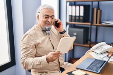 Orta yaşlı, kır saçlı, iş adamı. Ofiste akıllı telefondan not defteri okuyor.