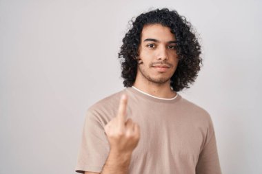 Hispanic man with curly hair standing over white background showing middle finger, impolite and rude fuck off expression 