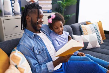 Father and daughter reading book sitting on sofa at home