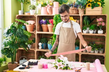 Young hispanic man florist smiling confident holding gift lace at flower shop