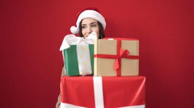 Güzel İspanyol kadın, Noel şapkası takıyor ve kırmızı arka planda hediyeler taşıyor.