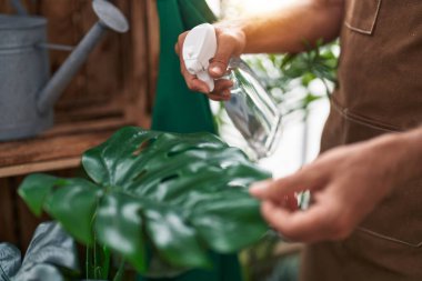 Young blond man florist watering plant working at flower shop