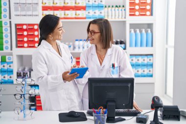 Two women pharmacist using computer and touchpad working at pharmacy