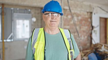 İnşaat alanında kendine gülen, orta yaşlı, gri saçlı bir inşaatçı.