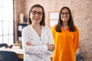 Two women business workers standing with arms crossed gesture at office