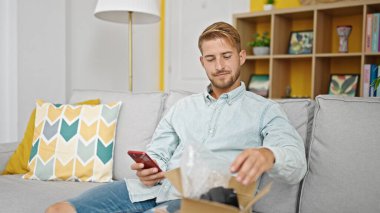 Kafkasyalı genç adam akıllı telefon kullanıyor. Evdeki karton kutuları açıyor.