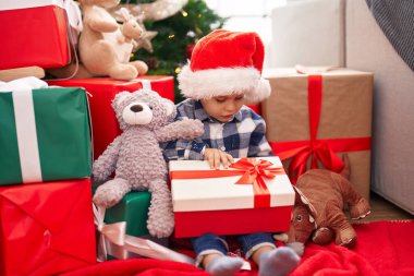 Sevimli bebek, evde yerde oturmuş Noel hediyesini açıyor.