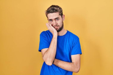 Sarı arka planda duran İspanyol sakallı adam çapraz kollu depresyon sorunlarından yorgun ve sıkılmış göründüğünü düşünüyor.. 