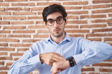 Tuğla duvarın arkasında dikilen genç İspanyol adam. Aceleyle saati, sabırsızlığı, son teslim tarihini geciktirdiği için üzgün ve kızgın olduğunu gösteriyor. 