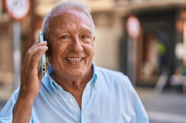 Senior grey-haired man smiling confident talking on the smartphone at street