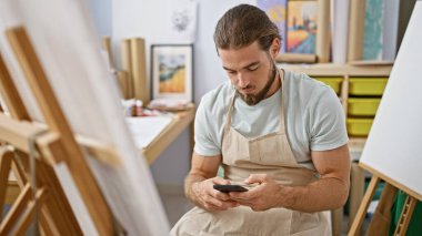 Genç İspanyol ressam sanat stüdyosunda akıllı telefon kullanıyor.