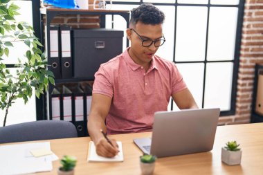 Genç Latin iş adamı ofisteki deftere dizüstü bilgisayar kullanıyor.