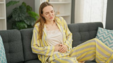 Adet sancısı çeken genç sarışın kadın evdeki kanepede oturuyor.