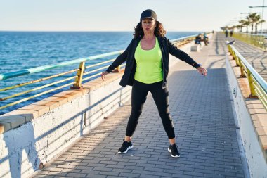 Middle age hispanic woman working out doing squats at promenade