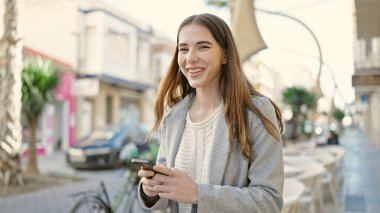 Kafe terasında gülümseyen akıllı telefon kullanan genç İspanyol kadın.