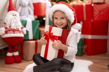 Sevimli İspanyol kız elinde hediyeyle evde Noel ağacının yanında oturuyor.