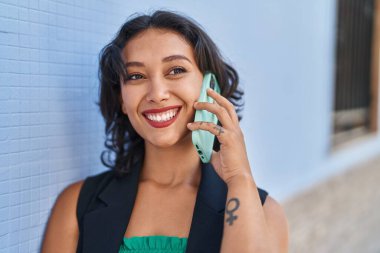 Genç, güzel, İspanyol bir kadın gülümsüyor ve caddede akıllı telefondan konuşuyor.