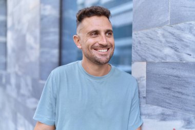 Young hispanic man smiling confident looking to the side at street