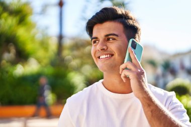 Genç İspanyol adam gülümsüyor. Parktaki akıllı telefondan konuşuyor.