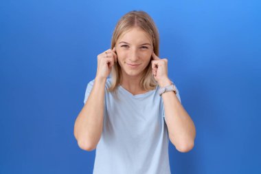 Gürültülü müzik sesi için kulaklarını parmaklarıyla kapatan günlük mavi tişört giyen genç beyaz kadın. sağır kavramı. 
