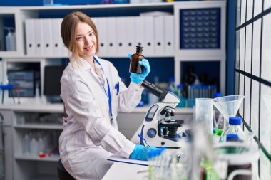 Young caucasian woman scientist write on document holding bottle at laboratory