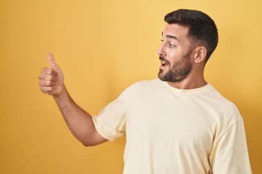 Sarı arka planda duran yakışıklı İspanyol adam. Gururlu görünüyor, gülümsüyor. Kenarda baş parmak hareketi yapıyor. 