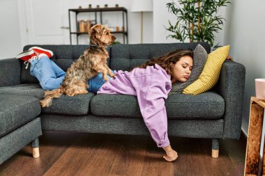 Genç, güzel, İspanyol bir kadın kanepede uzanıyor ve evde köpekle yatıyor.