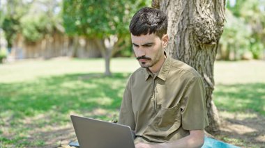 Genç İspanyol adam parkta dizüstü bilgisayar kullanıyor.