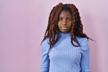 Pembe arka planda duran Afrikalı kadın yüzünde ciddi bir ifadeyle rahatlamış. Basit ve doğal bir şekilde kameraya bakıyorsun.. 