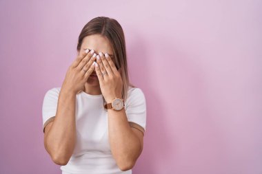 Sarışın, beyaz bir kadın pembe arka planda duruyor yorgunluk ve baş ağrısı için gözlerini ovuşturuyor, uykulu ve yorgun bir ifade. görme sorunu 
