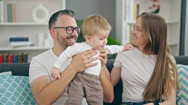 Anne, baba ve bebeğin ailesi evdeki kanepede otururken gülümsüyor.