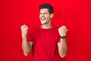 Young hispanic man standing over red background celebrating surprised and amazed for success with arms raised and eyes closed. winner concept. 