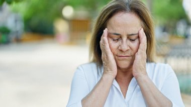 Orta yaşlı İspanyol kadın parkta baş ağrısı çekiyor.