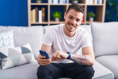 Genç İspanyol adam evde akıllı telefon kullanıyor.