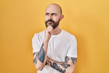 Sarı arka planda elleri çenesinde dikilen ve soru sormayı düşünen Latin kökenli genç bir adam, düşünceli bir ifade. Gülümseyen ve düşünceli bir yüz. şüphe kavramı. 