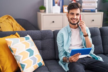 Genç İspanyol adam evde dokunmatik ped kullanarak akıllı telefondan konuşuyor.