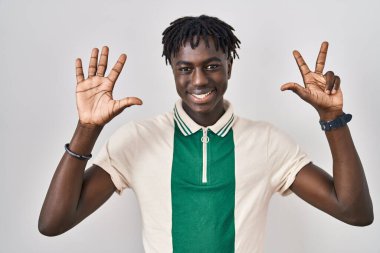 Münzevi arka planda dikilen Afrikalı adam 8 numaralı parmaklarıyla gülümseyerek kendinden emin ve mutlu bir şekilde işaret ediyor.. 