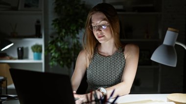 Genç sarışın iş kadını ofiste çalışırken laptop kullanıyor.