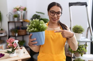 Çiçekçi dükkanında çalışan genç Arap kadın elinde saksıyla gülümsüyor. 