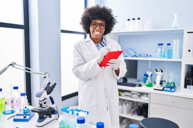 African american woman scientist smiling confident using touchpad at laboratory
