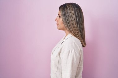 Pembe arka planda duran sarışın kadın yan bakıyor, rahat poz veriyor doğal bir yüz ve kendine güvenen bir gülümsemeyle.. 