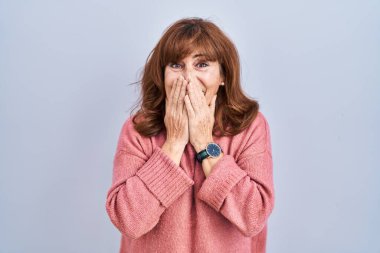 Orta yaşlı İspanyol bir kadın izole edilmiş arka planda durup gülüyor ve utanıyor kıkırdıyor elleriyle ağzını kapatıyor, dedikodu yapıyor ve skandal konsepti yapıyor. 