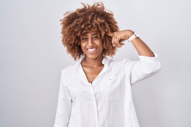 Beyaz arka planda duran kıvırcık saçlı, genç İspanyol kadın tek parmakla başını işaret ediyor, harika bir fikir ya da düşünce, iyi bir hafıza. 