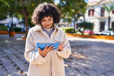 Genç, güzel, İspanyol bir kadın, gülümsüyor. Parktaki dokunmatik evde videolar izliyor.