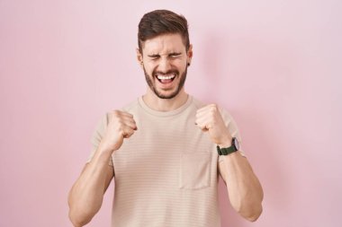 Hispanic man with beard standing over pink background excited for success with arms raised and eyes closed celebrating victory smiling. winner concept. 