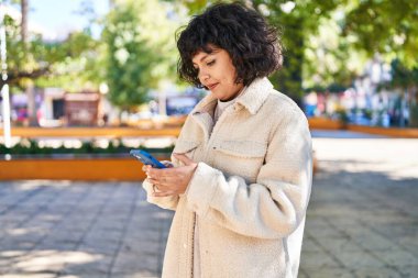 Parkta akıllı telefon kullanarak gülümseyen güzel bir İspanyol kadın.