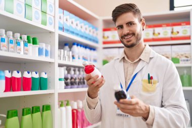 Young caucasian man pharmacist smiling confident holding medication bottles at pharmacy